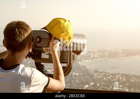 Ragazzo che guarda attraverso un binocolo a gettoni sulla Gelendzhik da una montagna vicina. Tonato. Foto Stock