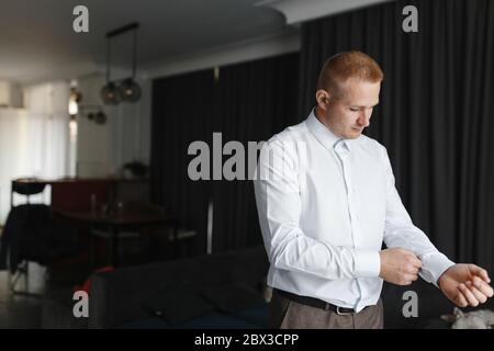 Uomo concentrato che fissa i bottoni sulle maniche della camicia. Preparazione dello sposo Foto Stock
