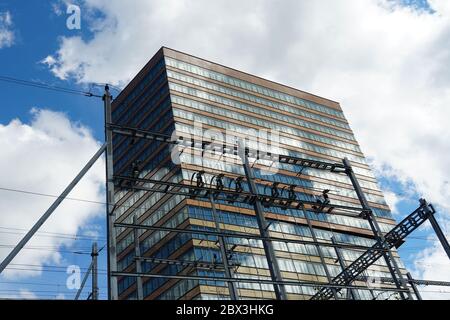 moderno edificio per uffici vicino a una stazione ferroviaria, la linea di contatto e i loro telai di supporto sono in primo piano. Foto Stock