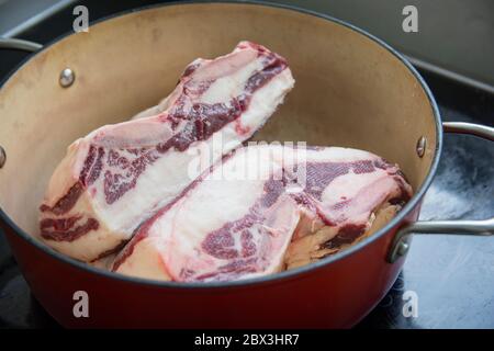 Scongelamento di due fette di carne di costolette corte in un pentolino rosso Foto Stock