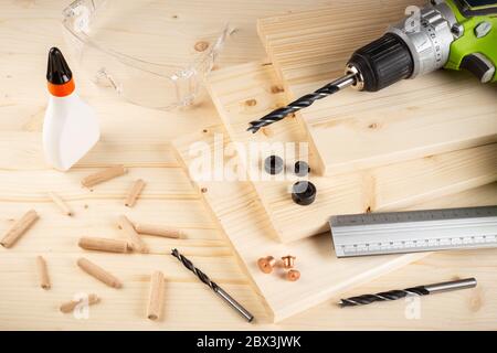 perni di giunzione in legno per punte di riferimento per trapano colla tavole di legno vetri di sicurezza cacciavite a batteria e utensili su fondo in abete rosso. Carpentiere industria funiture fare Foto Stock