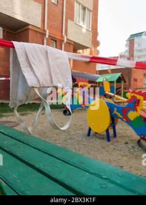 Maschera medica con nastro per barricata su un parco giochi chiuso per bambini in Russia. Concetto durante la pandemia di coronavirus della covid-19 Foto Stock