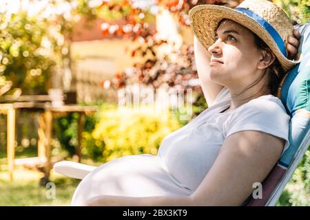 donna incinta che prende il sole in giardino in estate Foto Stock