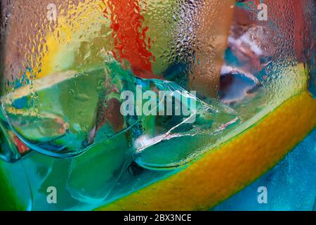 Sfondo astratto. Pezzi di ghiaccio in bevanda con limone. Foto macro. Retroilluminazione giallo blu neon, tè ghiaccio, whisky, Ice Cube, ghiaccio, cocktail Foto Stock