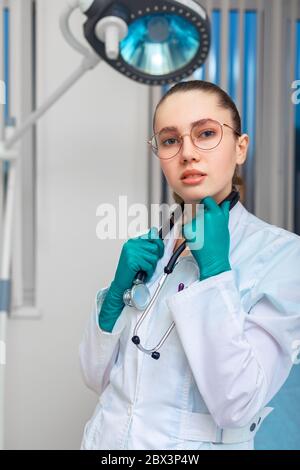 Medico in un cappotto bianco che tiene un fonendoscopio sullo sfondo di una stanza dell'ospedale. Medicina, salvavita, medici generici. Foto Stock