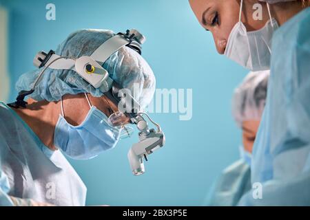 Primo piano nella sala operatoria, l'assistente consegna gli strumenti ai chirurghi durante il funzionamento. Intervento chirurgico in corso. Medici professionisti Foto Stock