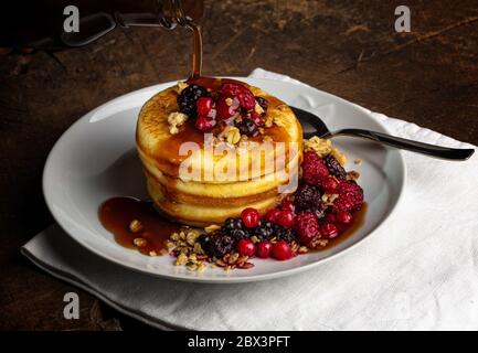 Primo piano di frittelle con frutti di bosco bacche su tavola di legno. Mirtilli, lamponi su frittelle con sciroppo d'acero. Concetto mattina proteine colazione Foto Stock