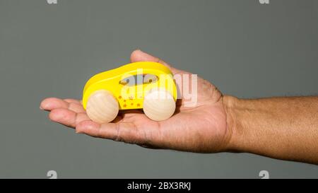 mano estensibile di un uomo nero con palmo in su che tiene un'automobile giocattolo gialla contro uno sfondo solido con spazio di copia Foto Stock