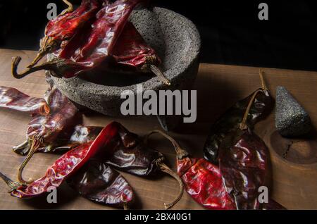 Cile Guajillo su una molcajete e su un tavolo di legno in un ambiente poco chiaro o luce chiave bassa, ingrediente per preparare la salsa come parte del cibo messicano. Foto Stock