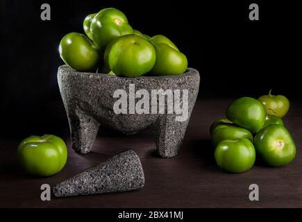 Un mazzo di Tomatillos o pomodoro di buccia in una molcajete in fotografia di cibo scuro su sfondo nero su un tavolo rustico di legno. Concetto di cibo messicano. Foto Stock