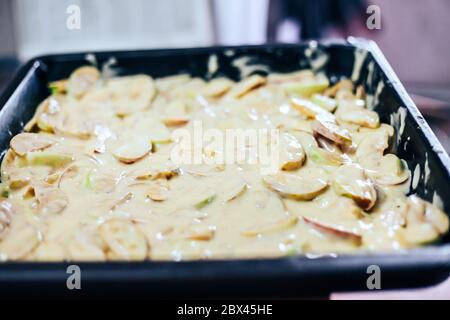 Torta di mele per la produzione a mano da donna. Primo piano. Impasto messo sulle mele Foto Stock