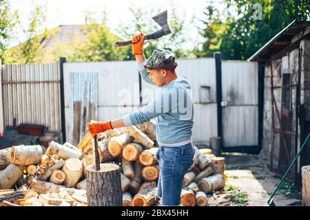 Uomo in jeans e camicia a scacchi in piedi vicino al moncone con ascia in mani Foto Stock