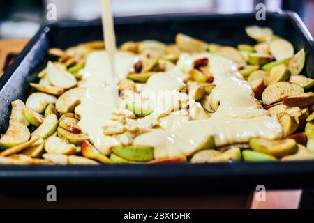 Torta di mele per la produzione a mano da donna. Primo piano. Impasto messo sulle mele Foto Stock