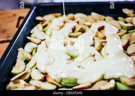 Torta di mele per la produzione a mano da donna. Primo piano. Impasto messo sulle mele Foto Stock