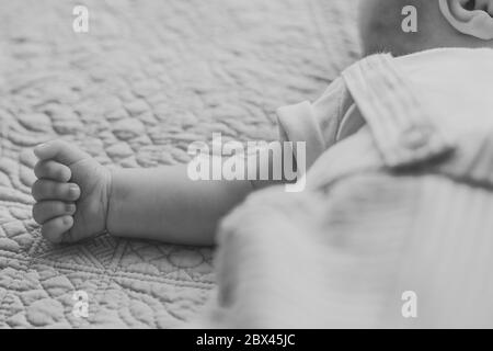 Bambino sdraiato sulla schiena sul letto all'interno con braccialetto al suo fianco in tute a righe Foto Stock