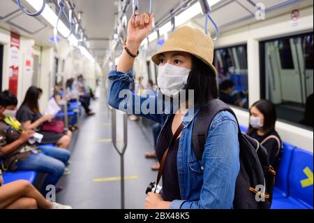 Donna asiatica che indossa una maschera medica monouso nel treno della metropolitana a Bangkok Foto Stock