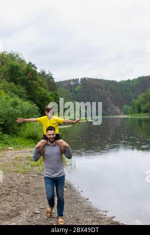 padre che dà il figlio piggyback cavalcare sulle spalle e ragazzo giocare aereo. Foto Stock