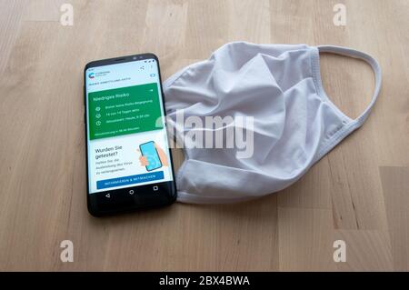 Zittau, Sassonia / Germania - 5 giugno 2020: Smartphone con analisi dei rischi risultato della tedesca Corona WARN Contact Tracing App con maschera bianca su woode Foto Stock