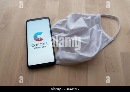 Zittau, Sassonia / Germania - 5 giugno 2020: Smartphone con schermo splash di Corona tedesco WARN contatto tracciatura App con maschera bianca su surfa in legno Foto Stock