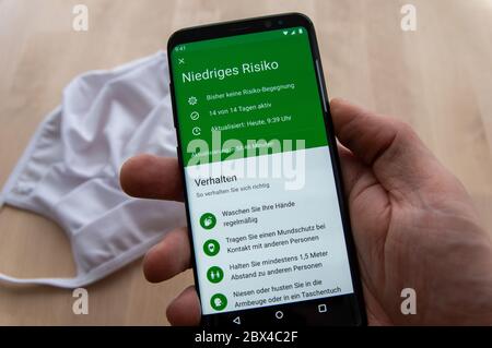 Zittau, Sassonia / Germania - 5 giugno 2020: Smartphone con tenuta a mano che mostra il risultato dell'analisi di rischio dell'applicazione tedesca Corona WARN con maschera bianca sfocata Foto Stock