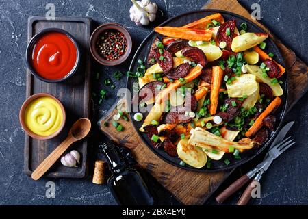 barbabietole arrosto a fette, spicchi di patate, pastinache, carote cosparse di cipolla verde tagliata su un asse di legno con ketchup, senape, vista orizzontale Foto Stock