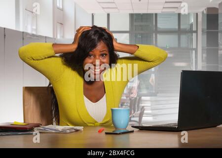 Giovane felice e attraente donna di affari afroamericana sorridente sicuro di lavoro alla scrivania del computer dell'ufficio in celebra riuscito dell'imprenditore Foto Stock