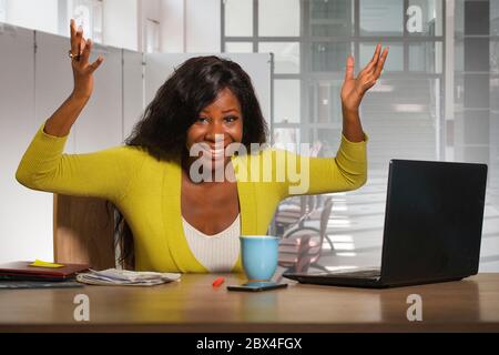 Giovane felice e attraente donna di affari americana afro nera sorridente sicuro di lavoro alla scrivania del computer dell'ufficio in celebratin riuscito dell'imprenditore Foto Stock