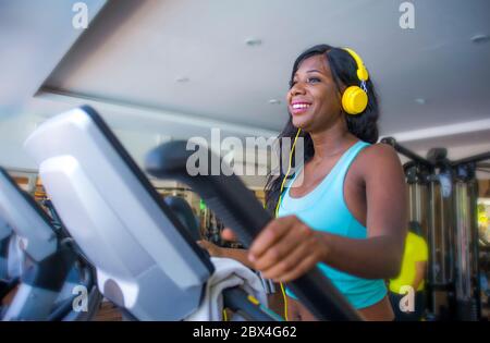 All'interno palestra ritratto di giovane attraente e felice donna afroamericana nera con cuffie allenamento ellittico macchina ginnica al fitness club SM Foto Stock