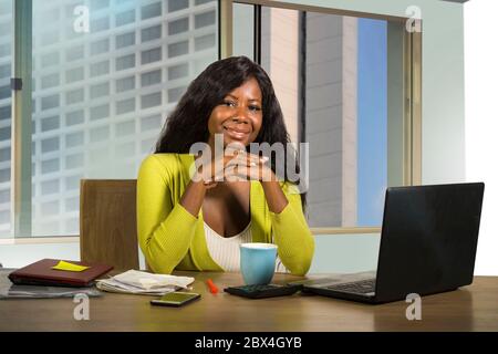 office ritratto aziendale di giovane felice e bella donna d'affari afroamericana nera che lavora fiducioso alla scrivania del computer sorridendo soddisfatto in fi Foto Stock