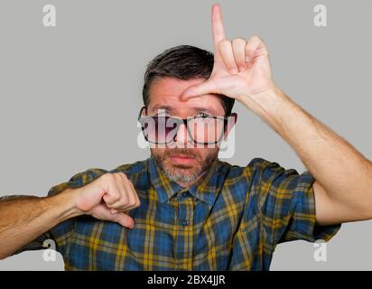 30s o 40s unshaven triste e vergognato uomo in strani vetri rotti nerdy facendo segno perdente con mano e dita sulla sua fronte con espr depresso divertente Foto Stock