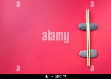 Disposizione piatta. I bastoncini di legno chiaro giacciono su pietre ovali su sfondo rosa. Posate tradizionali asiatiche. Spazio di copia Foto Stock