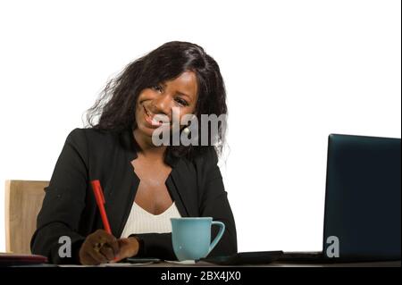 Giovane felice e attraente donna di affari afro americana nera che lavora alla scrivania del calcolatore d'ufficio sorridente riuscito che pone l'azienda come efficiente ed exp Foto Stock