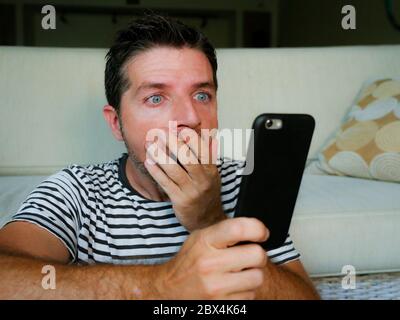 giovane uomo perplesso e scioccato utilizzando il telefono cellulare cercando internet social media o controllare le notizie in sorpresa e folle discredenza faccia espressione tassa Foto Stock