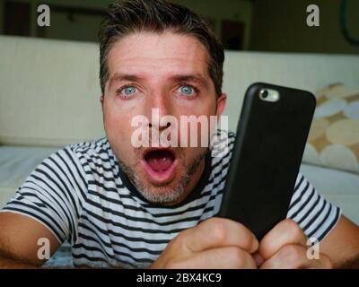 giovane uomo perplesso e scioccato utilizzando il telefono cellulare cercando internet social media o controllare le notizie in sorpresa e folle discredenza faccia espressione tassa Foto Stock