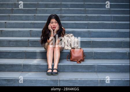 Giovane depressa e disperata donna asiatica d'affari americana piangendo da sola seduta su scala di strada che soffre stress e crisi di depressione essendo vict Foto Stock