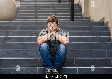 giovane uomo triste e disperato seduto all'aperto a scale di strada che soffrono l'ansia e la depressione sensazione misero piangendo abbandonato in disoccupazione e. Foto Stock