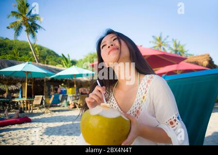 Giovane bella e felice asiatica coreana o cinese donna 20 bere rilassato succo di cocco sul paradiso tropicale resort sulla spiaggia in vacanze estive Foto Stock