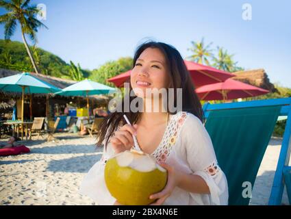 Giovane bella e felice asiatica coreana o cinese donna 20 bere rilassato succo di cocco sul paradiso tropicale resort sulla spiaggia in vacanze estive Foto Stock