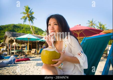 Giovane bella e felice asiatica coreana o cinese donna 20 bere rilassato succo di cocco sul paradiso tropicale resort sulla spiaggia in vacanze estive Foto Stock