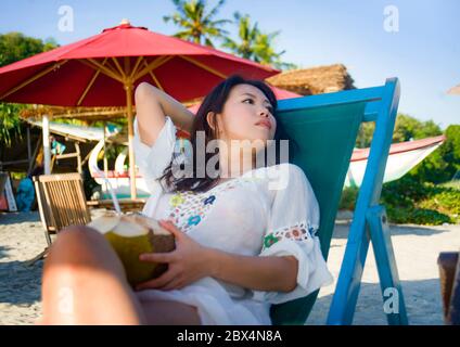 Giovane bella e felice asiatica coreana o cinese donna 20 bere rilassato succo di cocco sul paradiso tropicale resort sulla spiaggia in vacanze estive Foto Stock