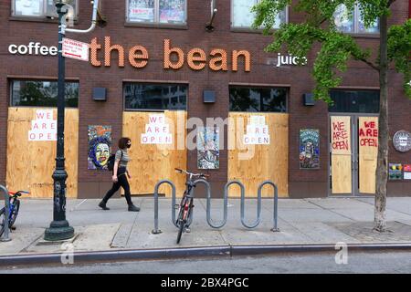 New York, 3 giugno 2020. Una persona con una maschera cammina davanti a una caffetteria con finestre chiuse e cartelli "We Are Open" dopo una recente ondata di furti/saccheggi organizzati su larga scala in altre parti della città. Il Bean si unisce ad altre aziende in tutta la città temendo i saccheggiatori salendo su finestre e porte come misura precauzionale e rimanendo aperto agli affari durante la pandemia di covid 19. I numerosi negozi chiusi in tutta la città inviano un messaggio di disperazione e disperazione a molti non abituati a vedere così tanti negozi chiusi in una città normalmente vivace e trafficata. Foto Stock