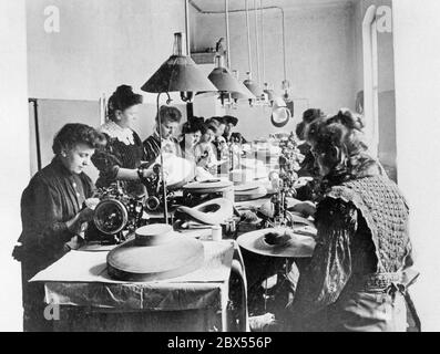 L'immagine del 1909 mostra le donne che lavorano alle loro macchine da cucire mentre fanno i cappelli di paglia. Le lampade a gas appendono al soffitto per illuminare la stanza. Foto Stock