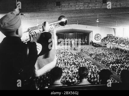 2000 educatori celebrano il decimo anniversario della NSLB ad Hof an der Saale, città fondatrice della Lega Nazionale Socialista per gli insegnanti (NS-Lehrerbund). Qui è mostrato il grande raduno nella Adolf Hitler Hall, dove il Ministro dell'Educazione del Reich Bernhard Rust ha pronunciato un discorso sui principi dell'impegno politico degli educatori (sullo sfondo della scena al leggio). In primo piano un ragazzo della gioventù Hitler sta suonando la tromba. Foto Stock