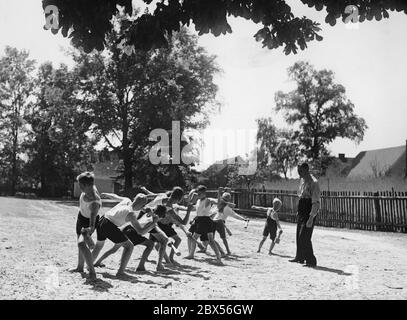 I ragazzi gettano le granate a mano in legno come esercizio fisico durante le lezioni di ginnastica in una scuola di villaggio, sotto la supervisione di un insegnante. Foto Stock