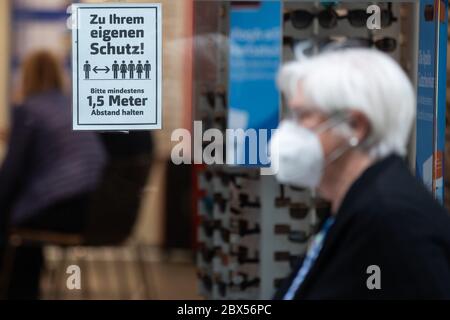 05 giugno 2020, Baden-Wuerttemberg, Stoccarda: Una donna che indossa un boccaglio cammina con un cartello che dice 'per la vostra protezione! Si prega di mantenere una distanza di almeno 1.5 metri, che è bloccato in una vetrina. Foto: Tom Weller/dpa Foto Stock