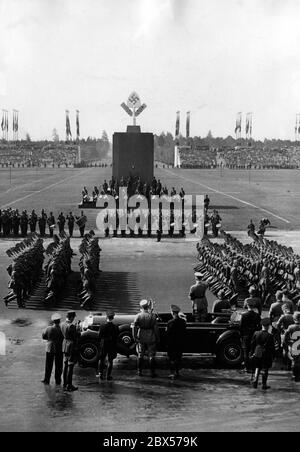 Adolf Hitler, in piedi in una Mercedes sullo Zeppelinwiese, prende il saluto delle formazioni del Reich Labour Service marciando con le loro vortici. Sullo sfondo, gruppi di batteristi e il Memoriale del lavoro. Foto Stock