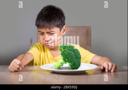 8 anni disgustato e dispiaciuto bambino rifiutando di mangiare sano verde broccoli sensazione di sconvolto in educazione alimentare bambino su cibo sano fresco e y Foto Stock