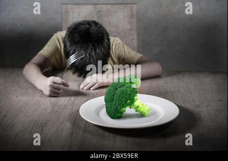 8 anni disgustato e dispiaciuto bambino rifiutando di mangiare sano verde broccoli sensazione di sconvolto in educazione alimentare bambino su cibo sano fresco e y Foto Stock