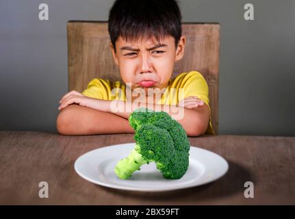 8 anni disgustato e dispiaciuto bambino rifiutando di mangiare sano verde broccoli sensazione di sconvolto in educazione alimentare bambino su cibo sano fresco e y Foto Stock