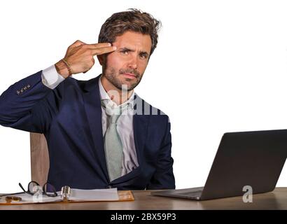 giovane uomo d'affari triste e depresso che lavora sopraffatti e frustrato sulla scrivania del computer portatile ufficio che si sente sconvolto e stressato puntando la pistola a mano fi Foto Stock